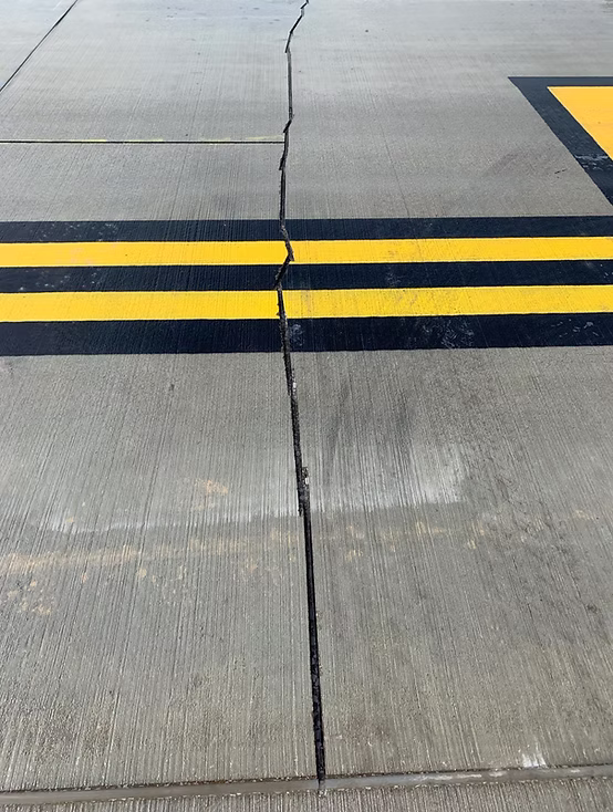 Repaired crack sealed with black filler running across a concrete slab and crossing double yellow line markings