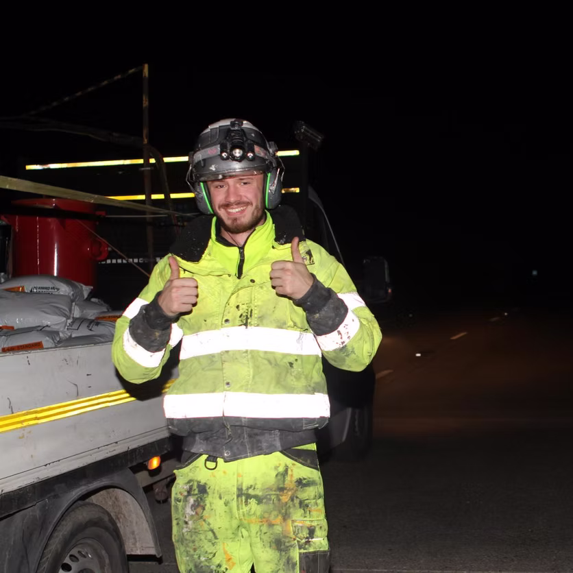 Worker in yellow hi-vis coveralls standing beside a truck at night