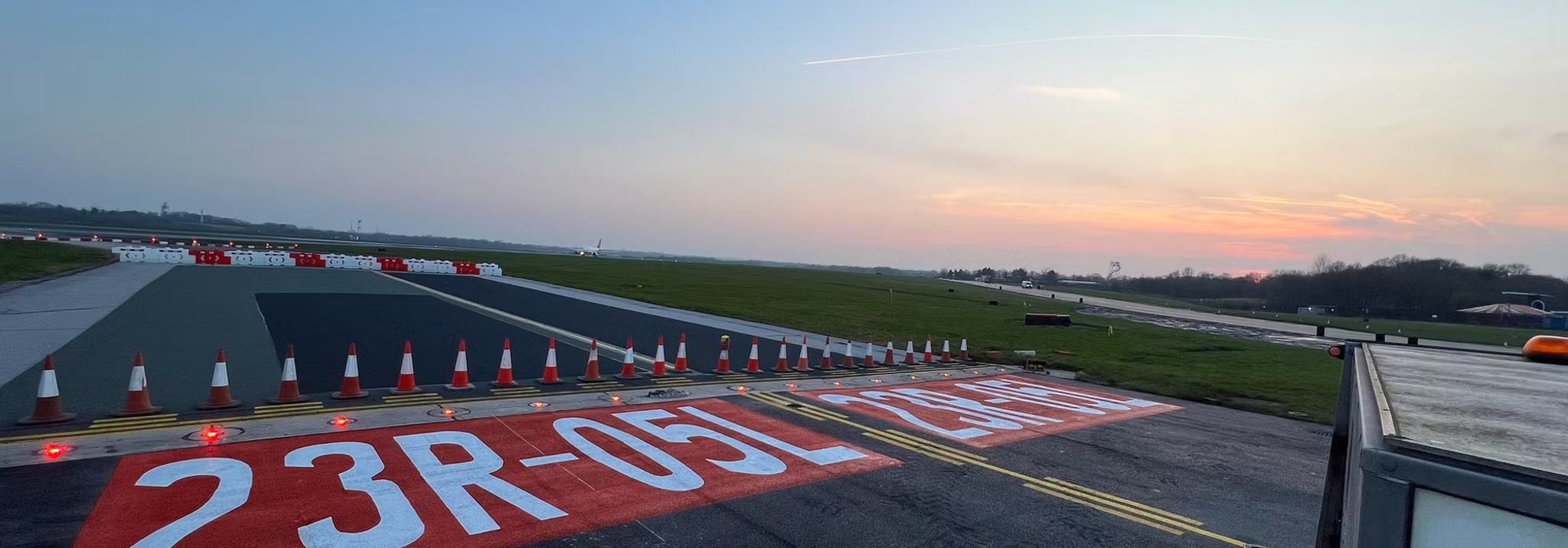 Runway threshold with a large red and white 23R-05L designation marking lined with traffic cones at dusk