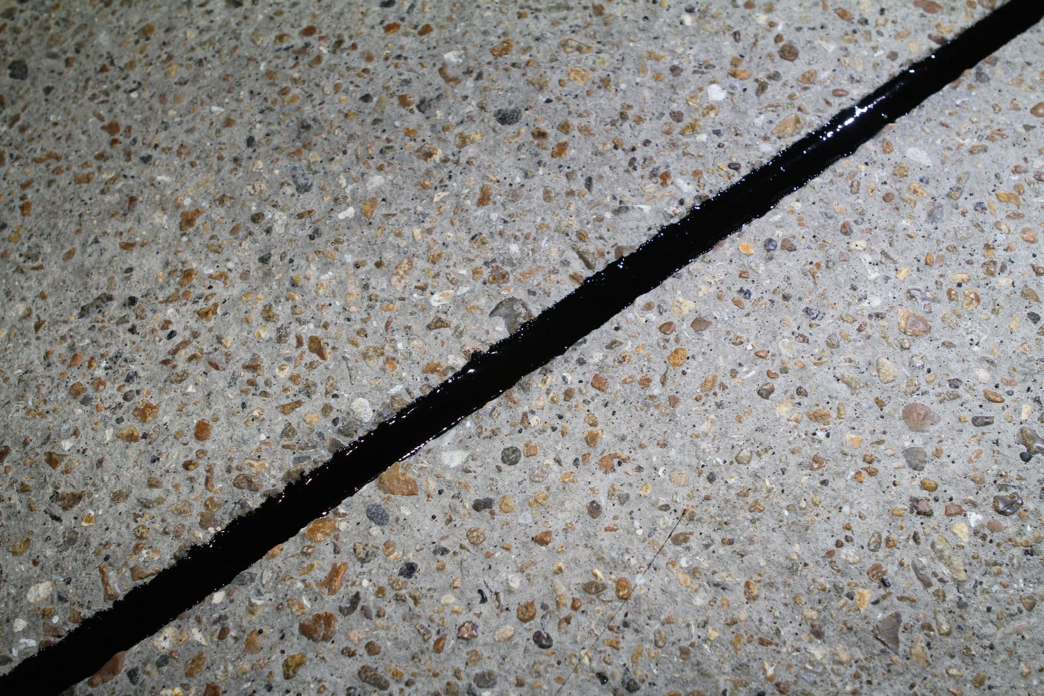 A black hot applied sealant bead filling a joint across an exposed aggregate concrete slab
