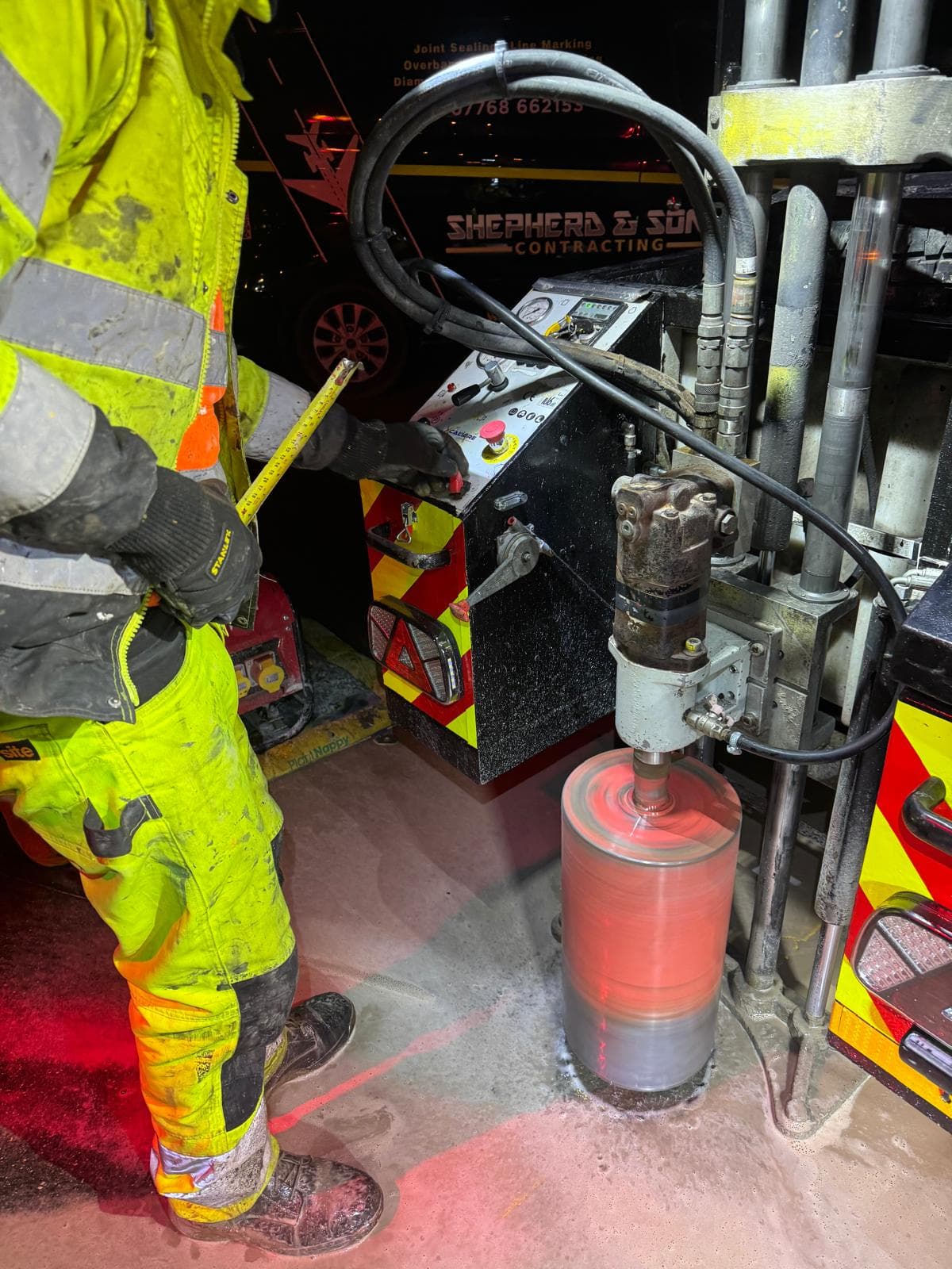 Worker in hi-vis operating a core-drilling rig with a hydraulic power pack at night beside a branded Shepherd and Sons machine