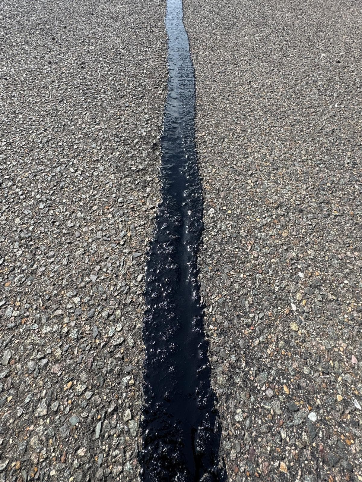 Close-up of a crack in a tarmac surface filled with black sealant