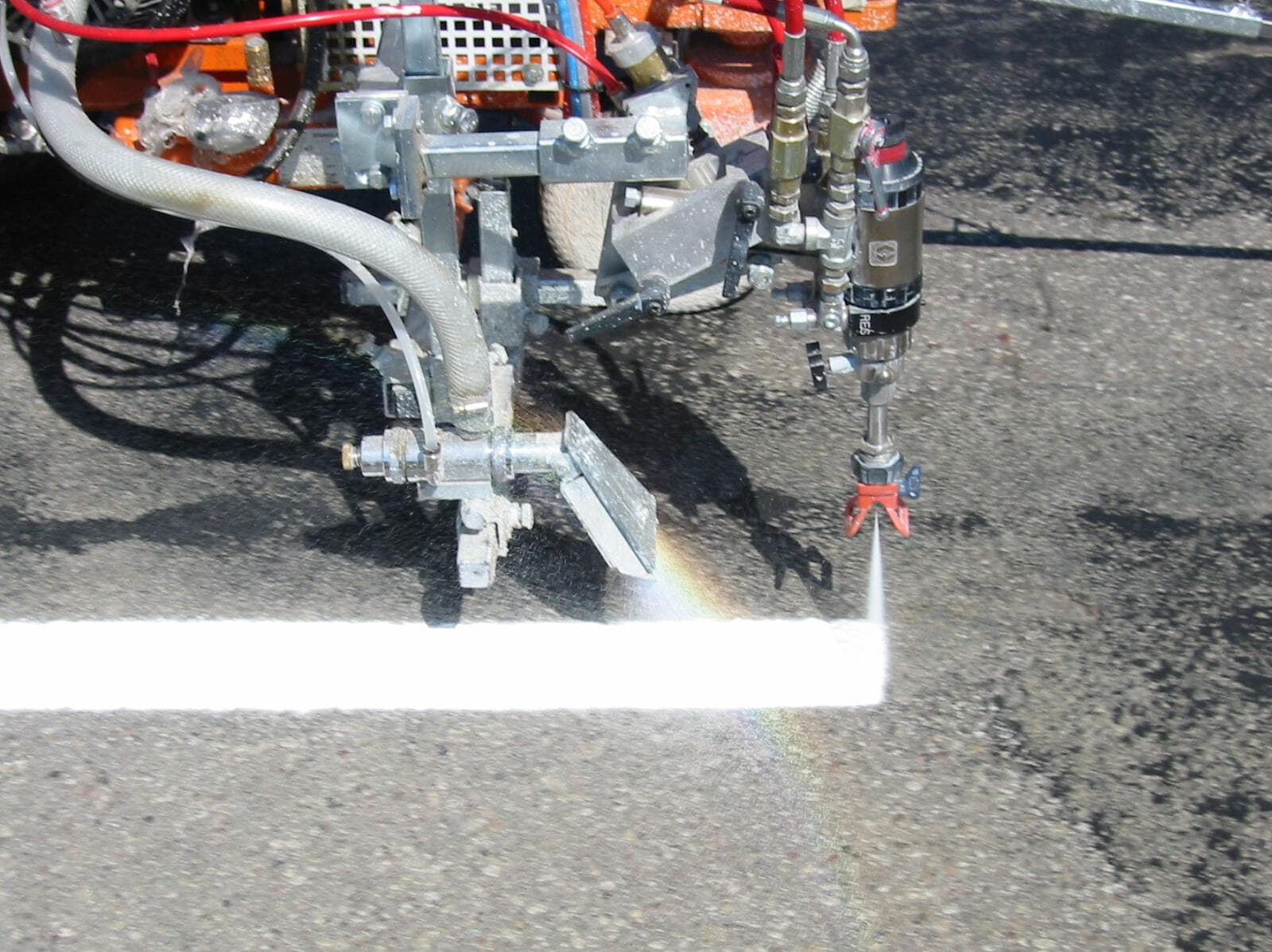The spray head of a line marking machine laying a fresh white line onto asphalt
