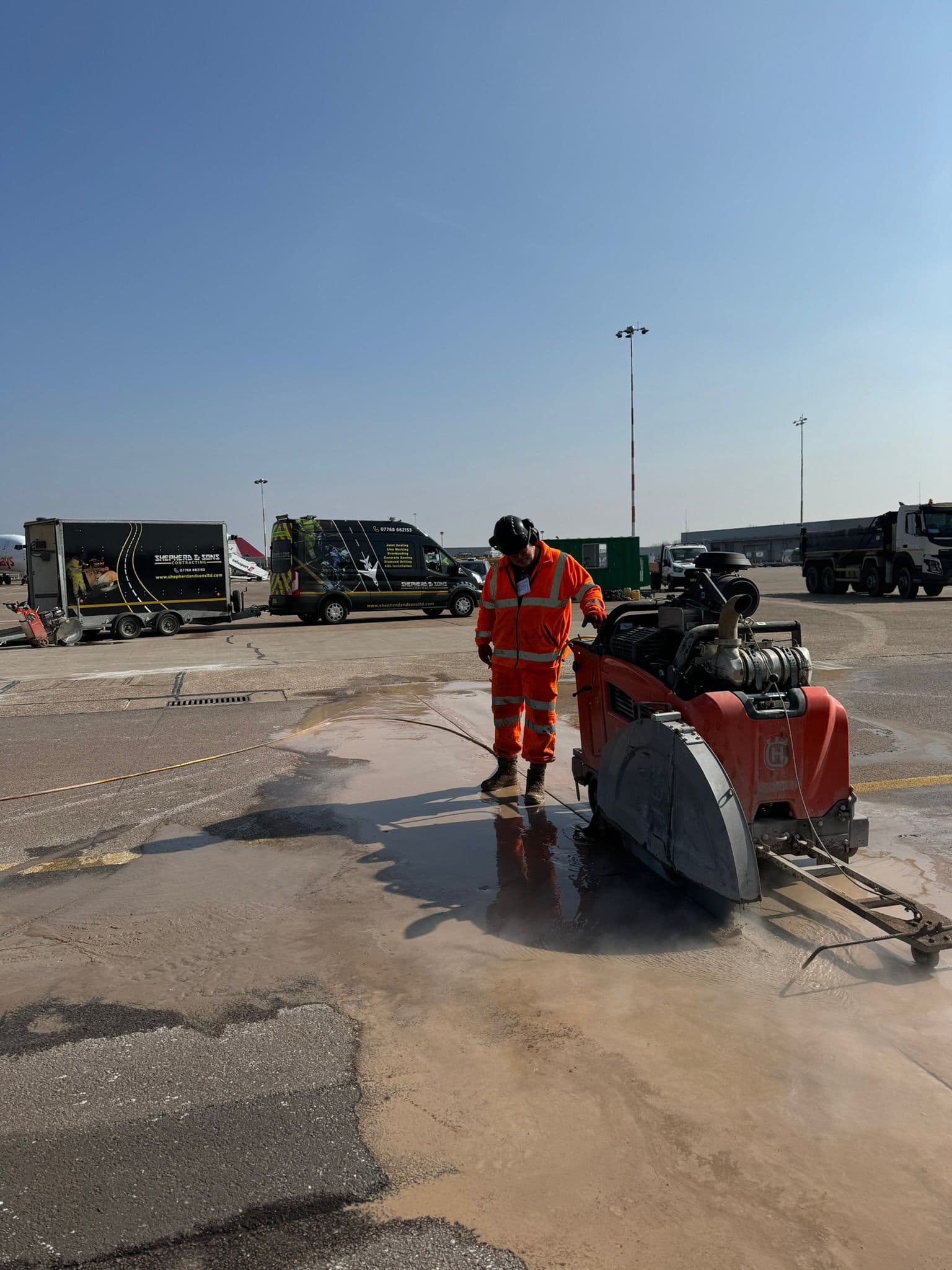 Worker in hi-vis operating a walk-behind floor saw on an airfield apron with a branded Shepherd and Sons van behind