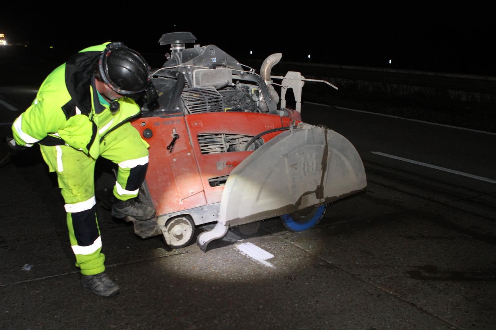 Worker in hi-vis and ear defenders operating a large walk-behind floor saw with a big blade on a road at night