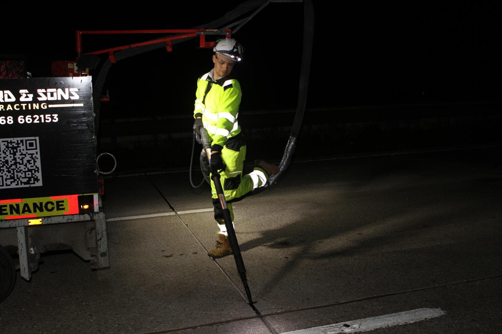 Worker in hi-vis using a lance on a road joint at night beside a branded Shepherd and Sons maintenance trailer