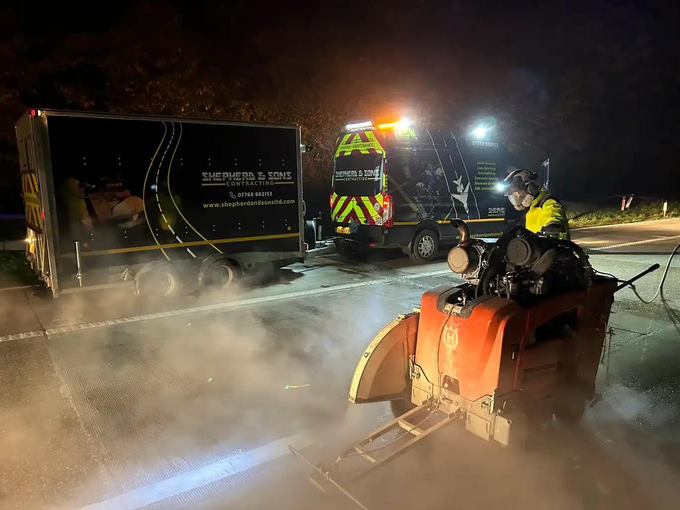 An operative cutting a chase into a road at night, with the Shepherd and Sons van and trailer lit behind