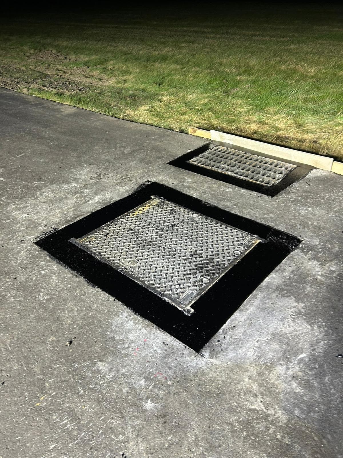 Two metal access covers set into a concrete surface with black bituminous sealant around their frames