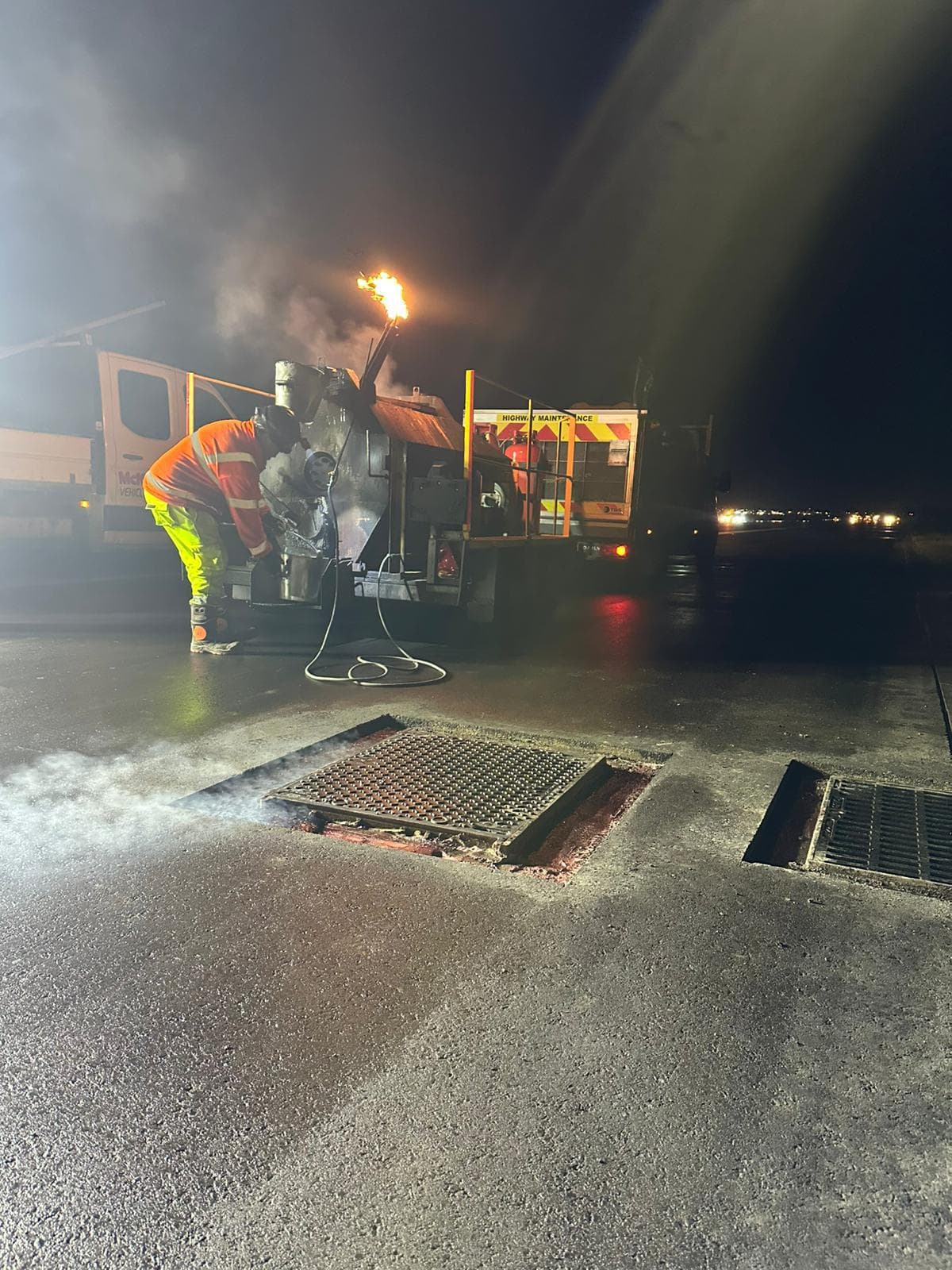 Operative in hi-vis tending a bitumen boiler with an open flame on a Highway Maintenance truck at night