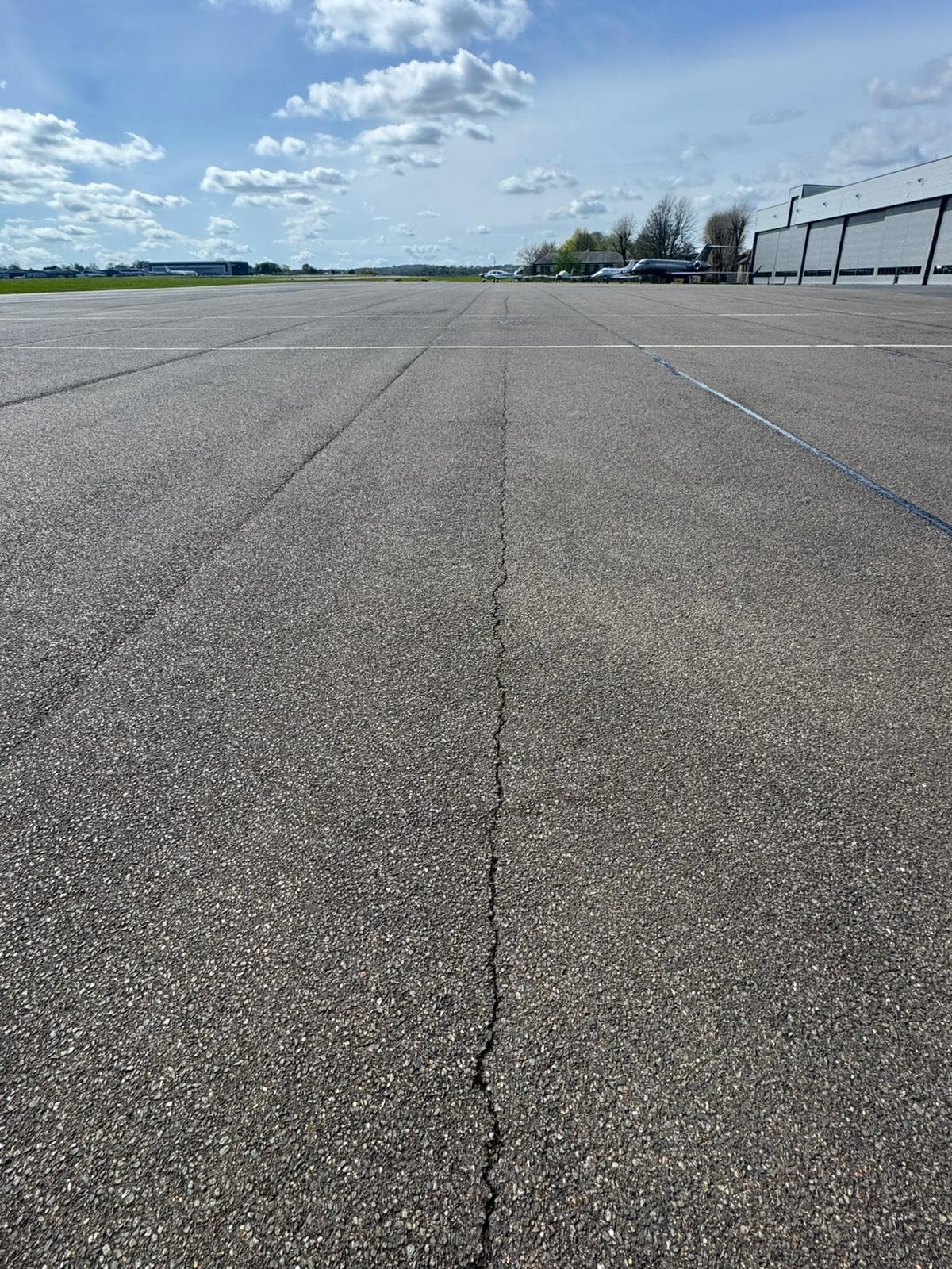 Wide low-angle view of a cracked concrete apron with parked aircraft and hangars in the distance