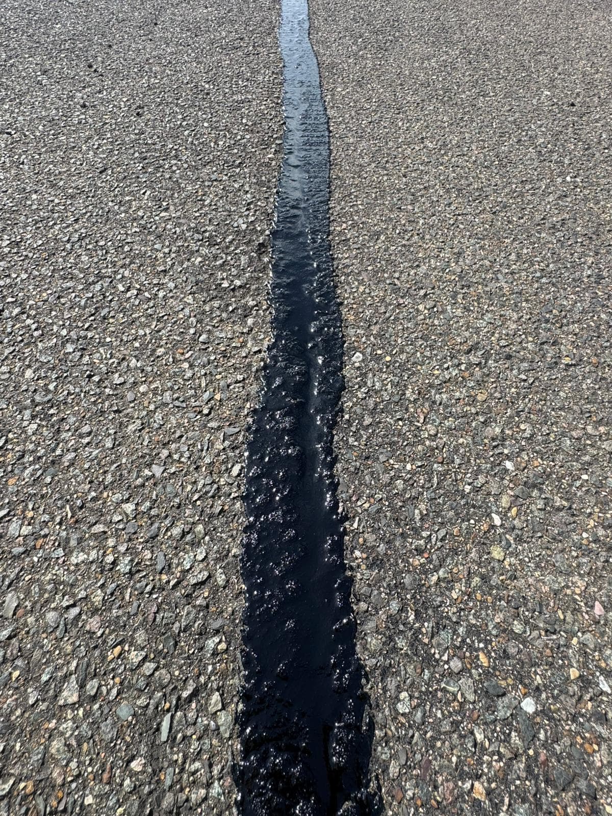 Close-up of a single crack in a grey aggregate road surface freshly filled with black bituminous sealant