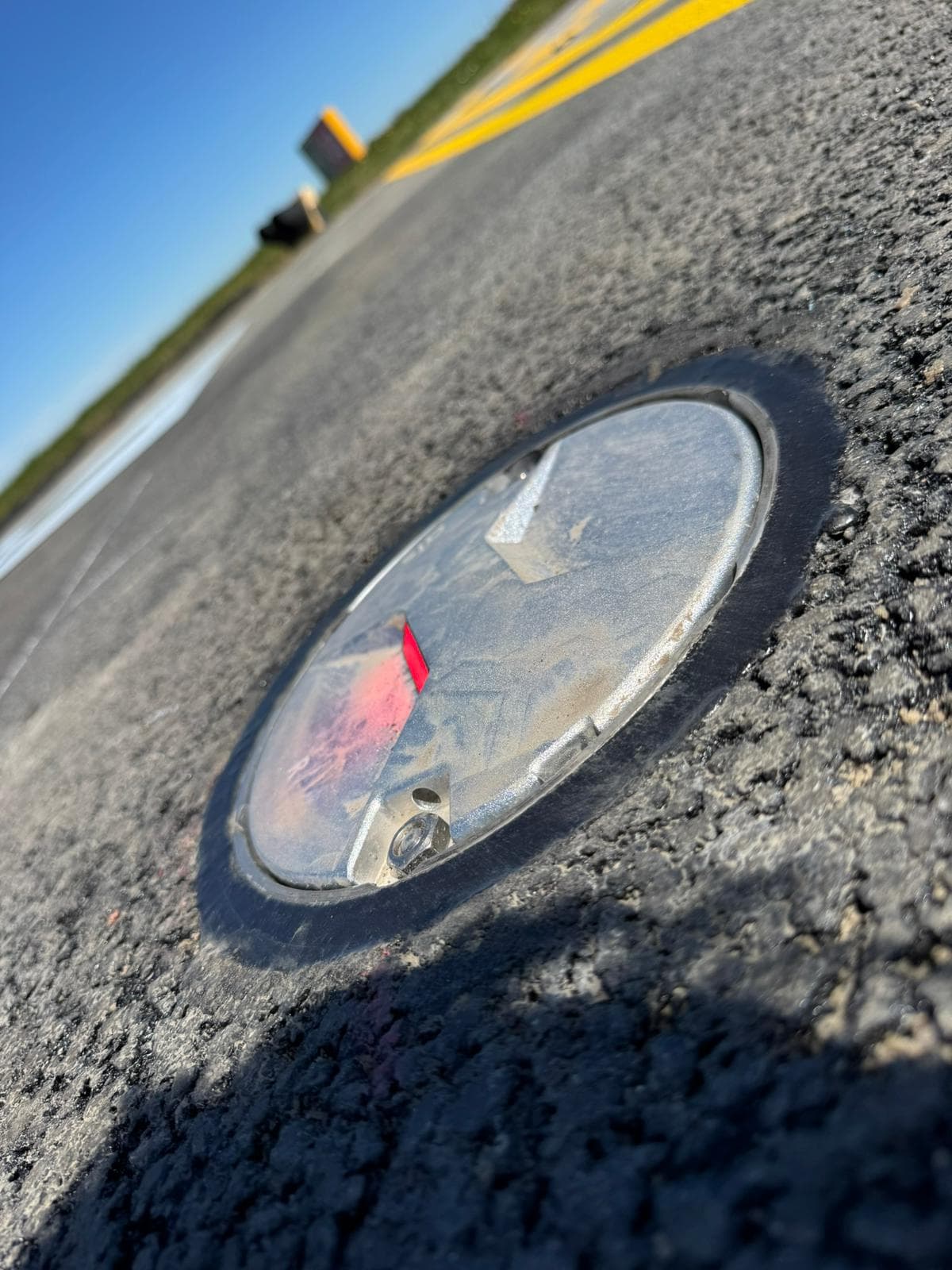 Close-up of a circular metal inspection cover set flush into a tarmac surface and sealed around the edge