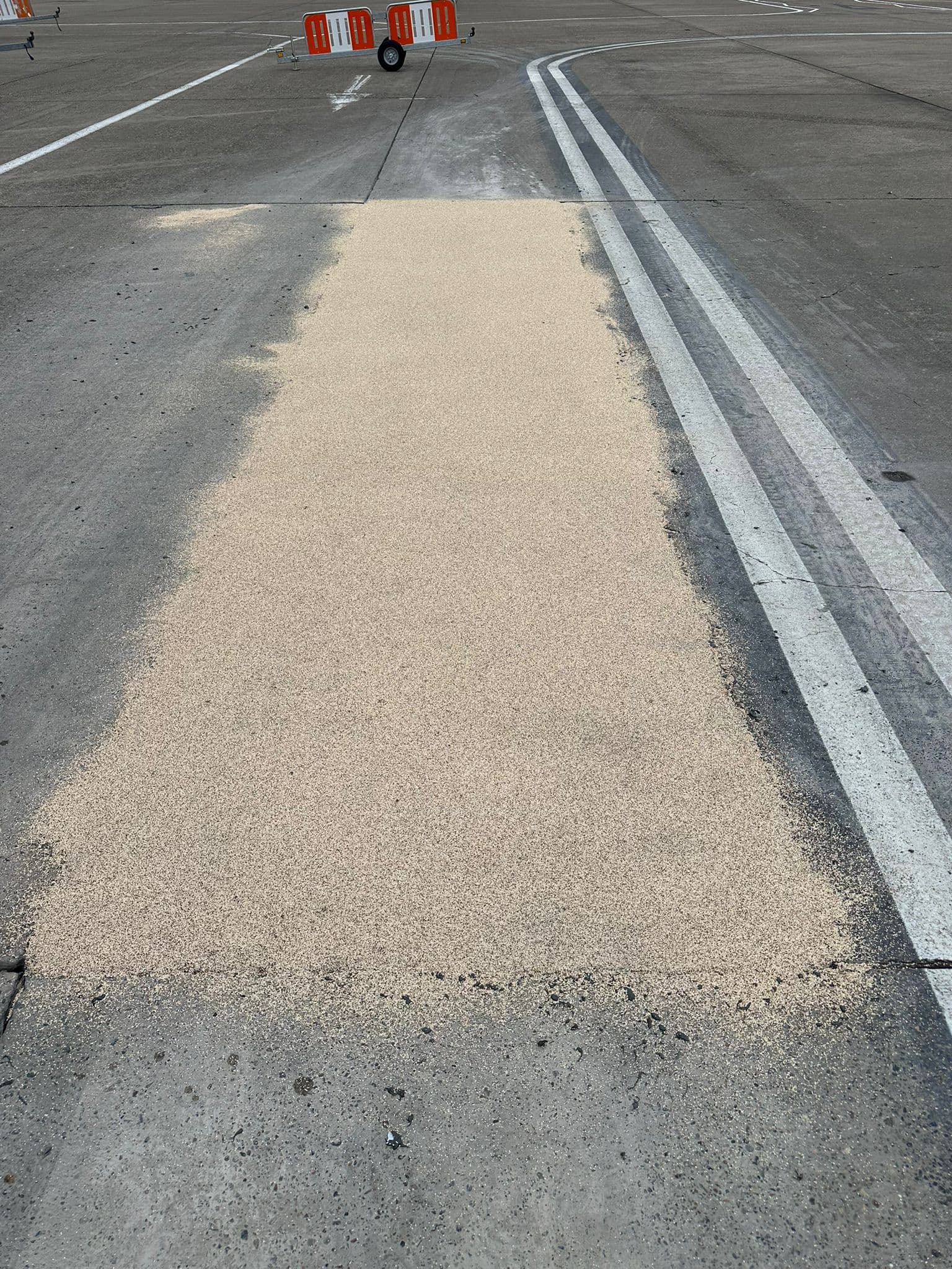 Strip of pale buff high-friction anti-skid surfacing applied to a grey asphalt surface beside white line markings