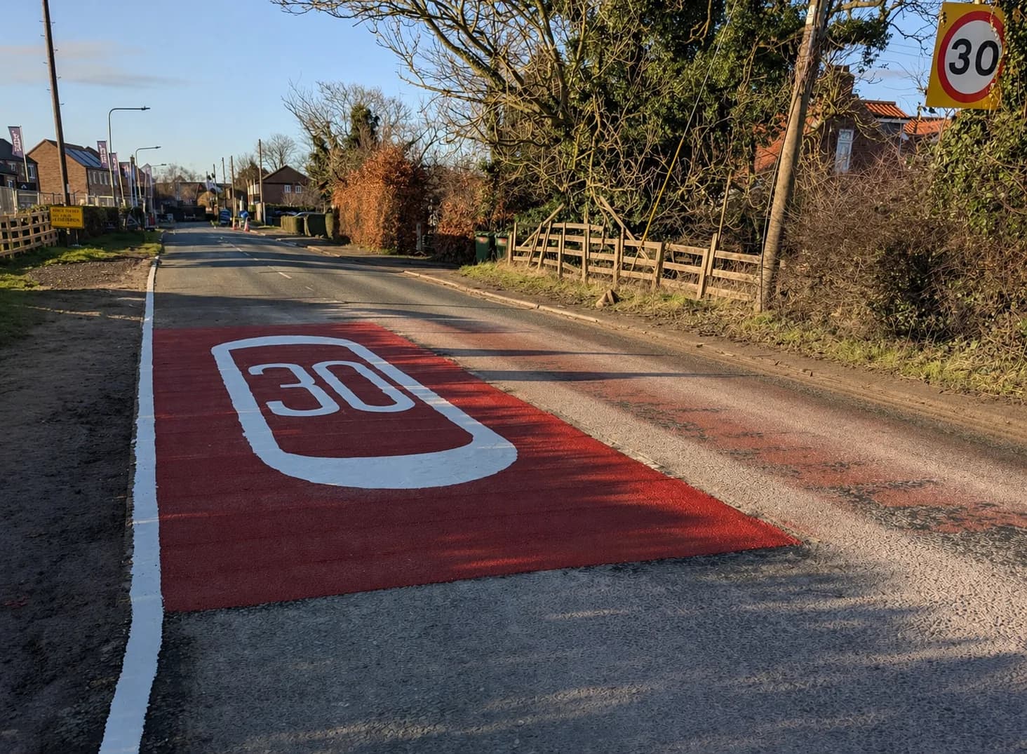Red anti-skid road surfacing with a large white 30 speed limit roundel on a residential street