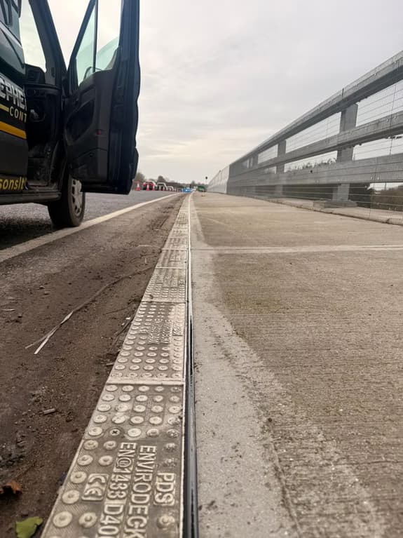 Close-up of a newly installed linear slot drainage channel alongside a concrete road with a crash barrier