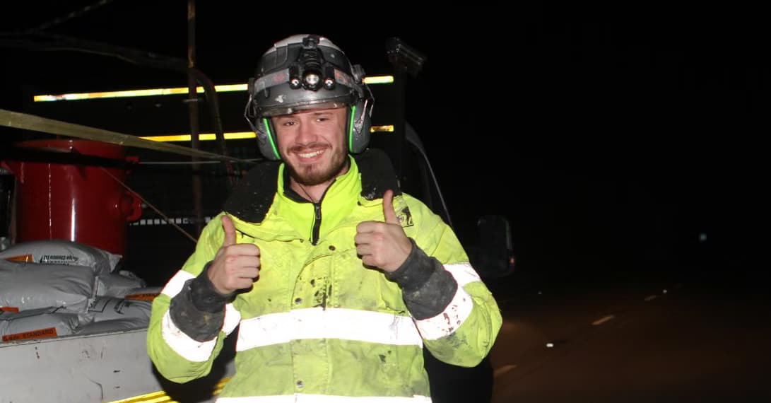 Worker in yellow hi-vis, hard hat and ear defenders giving a double thumbs-up at night