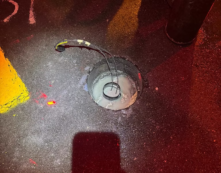 Overhead view of an open inspection chamber with a coiled hose inside on a road with yellow markings