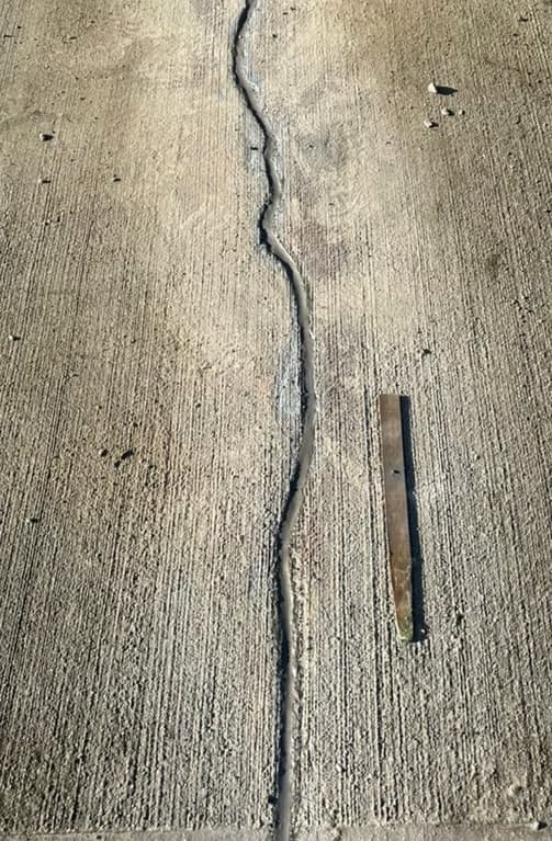 Close-up of a crack running across a concrete slab surface with a tool laid alongside for scale