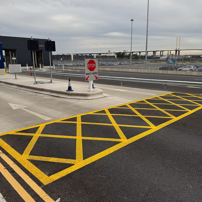 Freshly painted yellow hatched road markings leading to a STOP and wait here sign and traffic cone