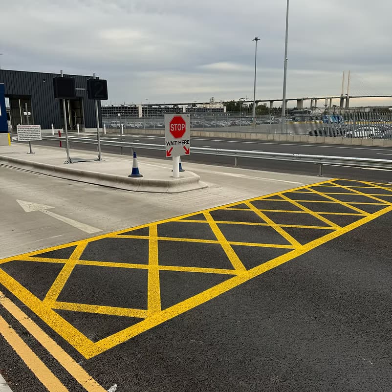 Freshly painted yellow hatched road markings leading to a STOP and wait here sign and traffic cone