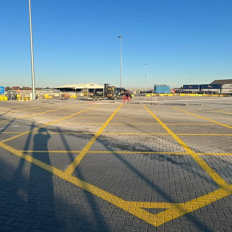 Block-paved yard with freshly painted yellow bay markings, containers and industrial buildings behind