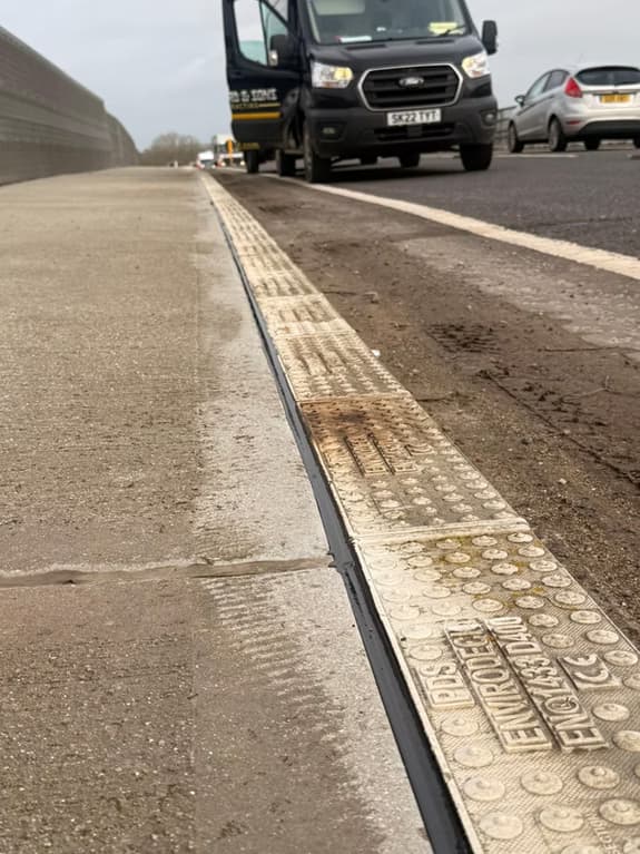 Linear slot drainage channel running along the edge of a road beside white line markings