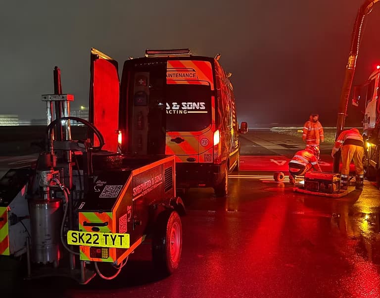 Shepherd and Sons Contracting trailer and van at a night work site in red light with workers on a wet road