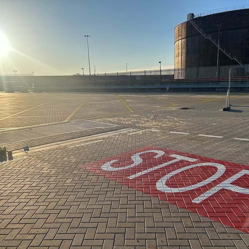 Large red STOP road marking painted on block-paved ground at a fenced yard in bright sunlight