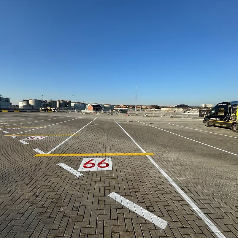 Block-paved apron with a large red 66 bay number and white and yellow markings, a van and storage tanks behind