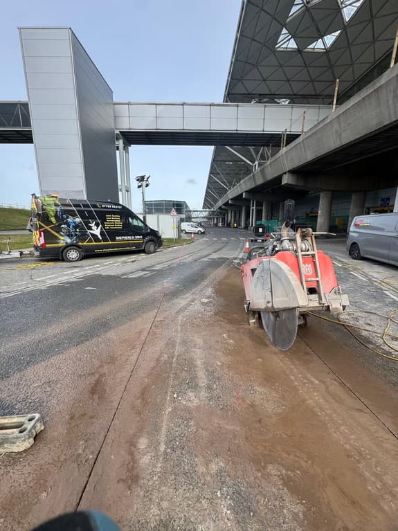 Red road saw and a Shepherd and Sons Contracting van beneath a raised motorway flyover in daytime