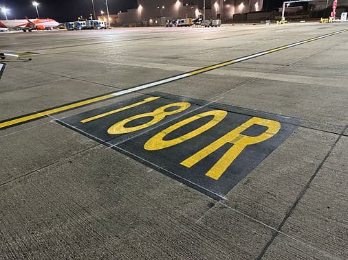 Yellow 180R runway designation marking painted on a tarmac surface
