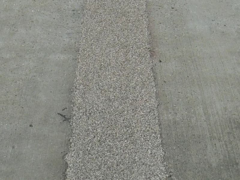 Close-up of a lighter cementitious repair strip set into a darker aggregate paved surface