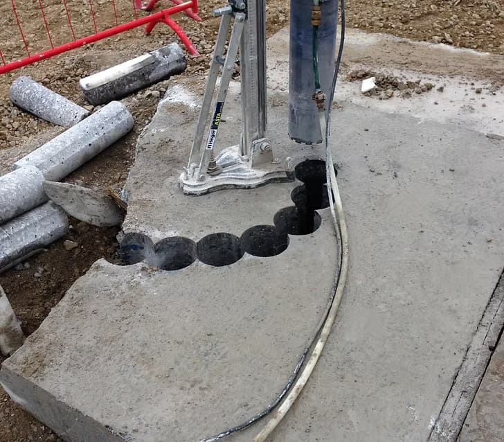 Curved line of overlapping core-drilled holes through a concrete slab with a core drill rig nearby