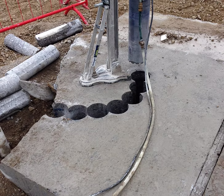 Curved line of overlapping core-drilled holes through a concrete slab with a core drill rig nearby