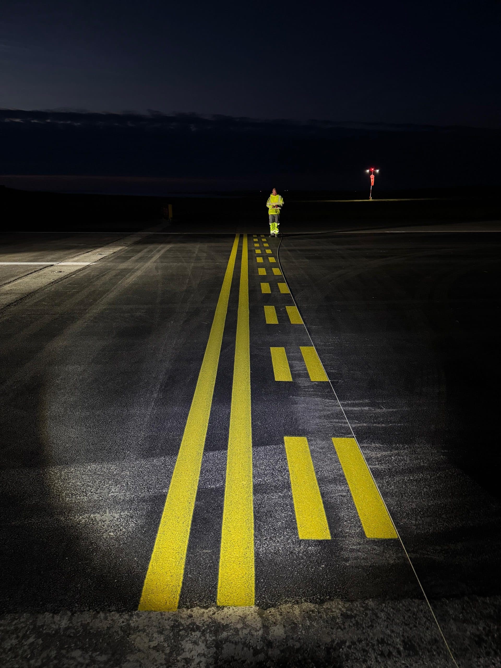 Freshly painted yellow taxiway markings on a runway at night with a worker in hi-vis
