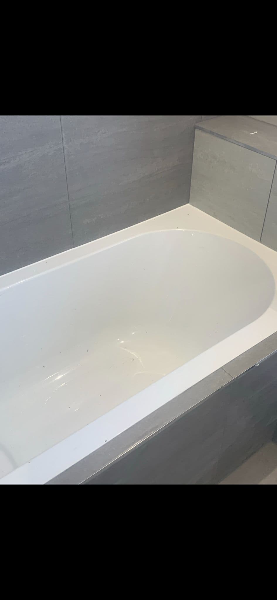 White bath edge sealed with silicone along the join with grey tiled walls