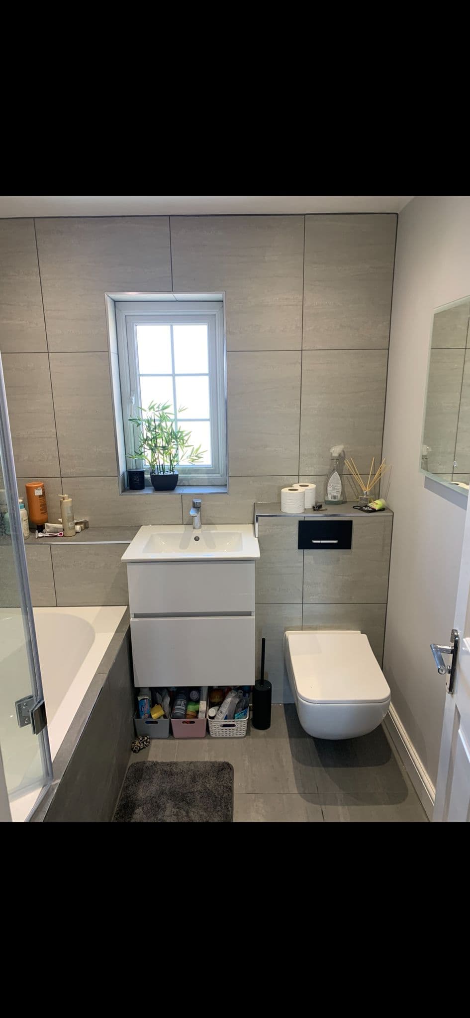 Tiled bathroom wall with a frosted window, plant on the sill and a mirror alongside