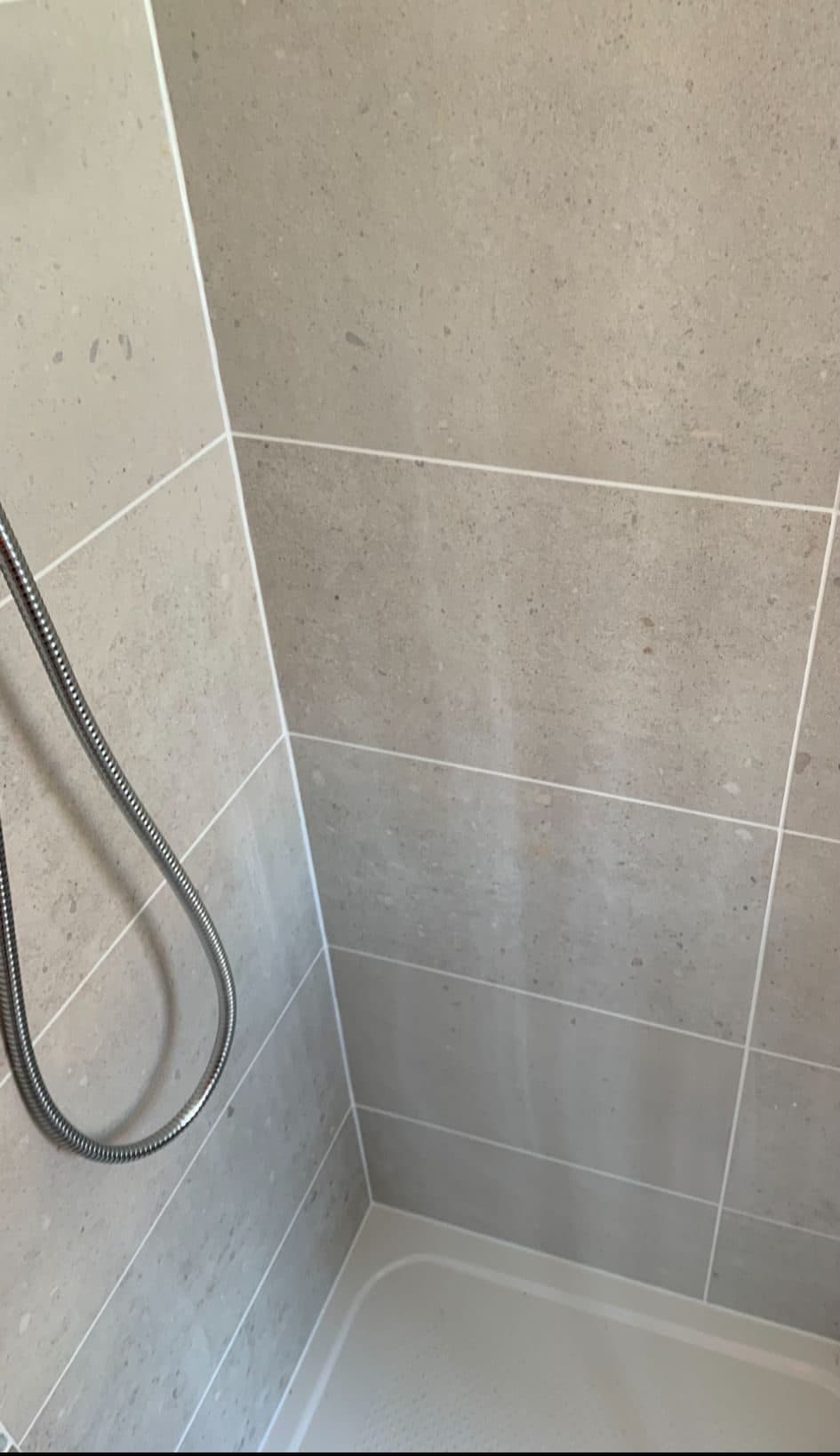 Corner of a tiled shower with beige stone-effect tiles, grout lines and a shower hose