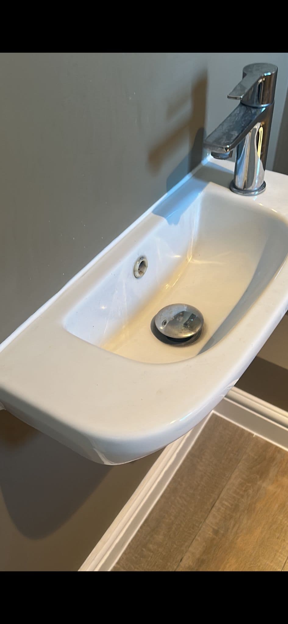 White basin with a chrome tap, sealed with silicone along the join with the wall