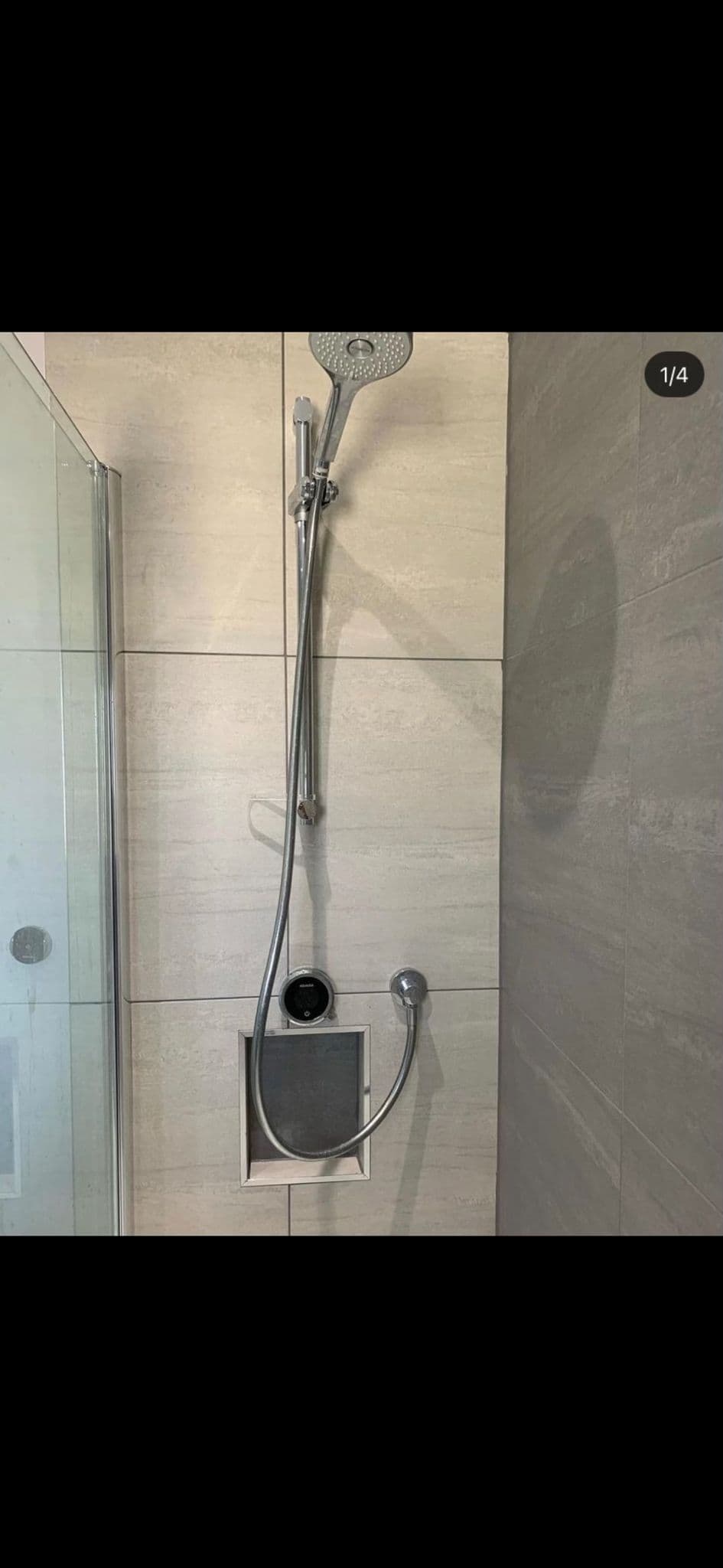 Chrome shower riser and heads in a glass shower against beige stone-effect tiles