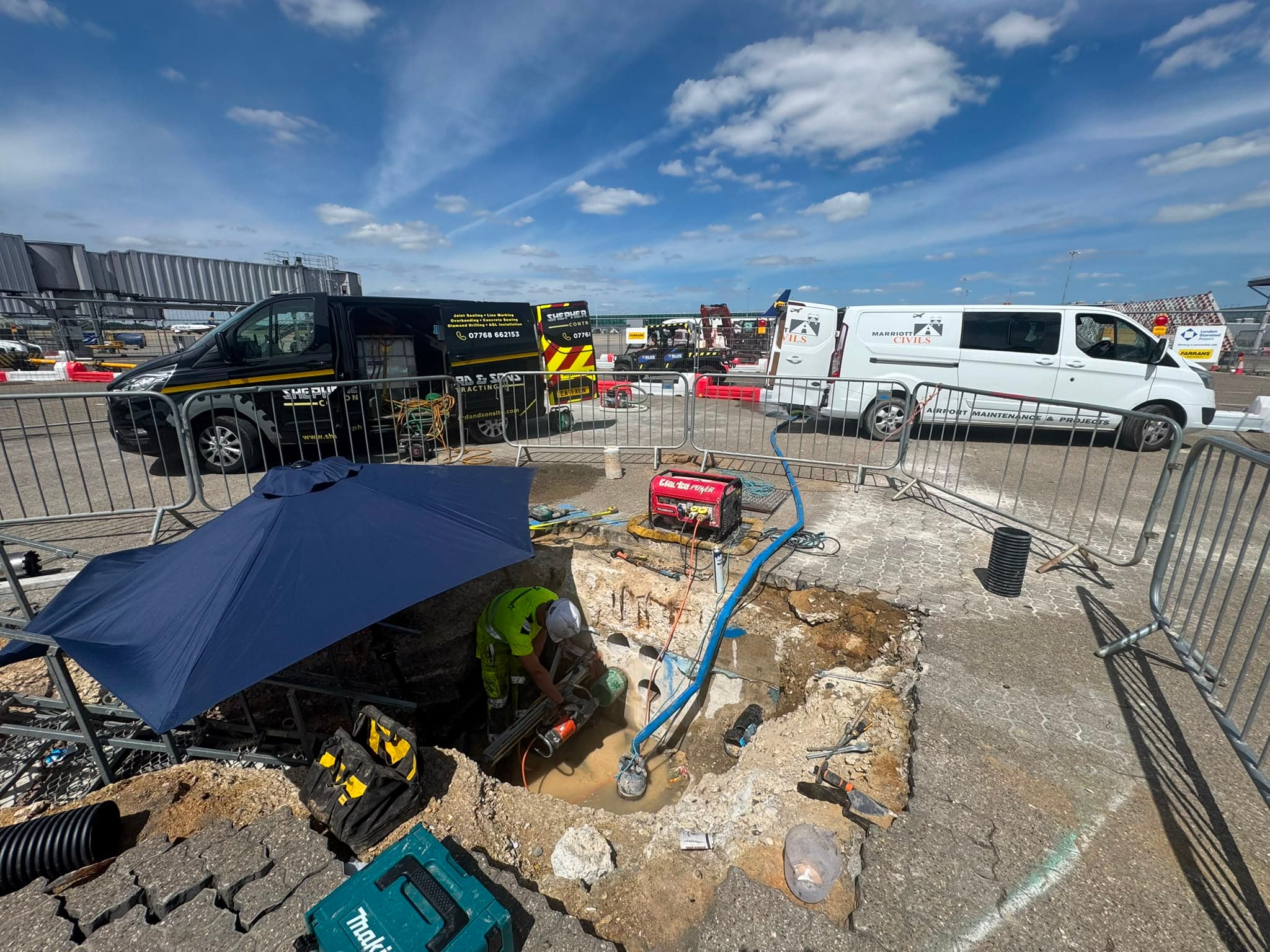 Worksite with Shepherd and Sons and Marriott Civils vans behind fencing, a worker, generator and hoses