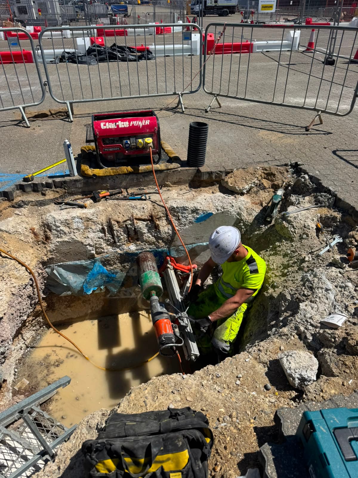 Excavation on a construction site with a Stanley tool bag, Makita case and a red generator beside metal fencing