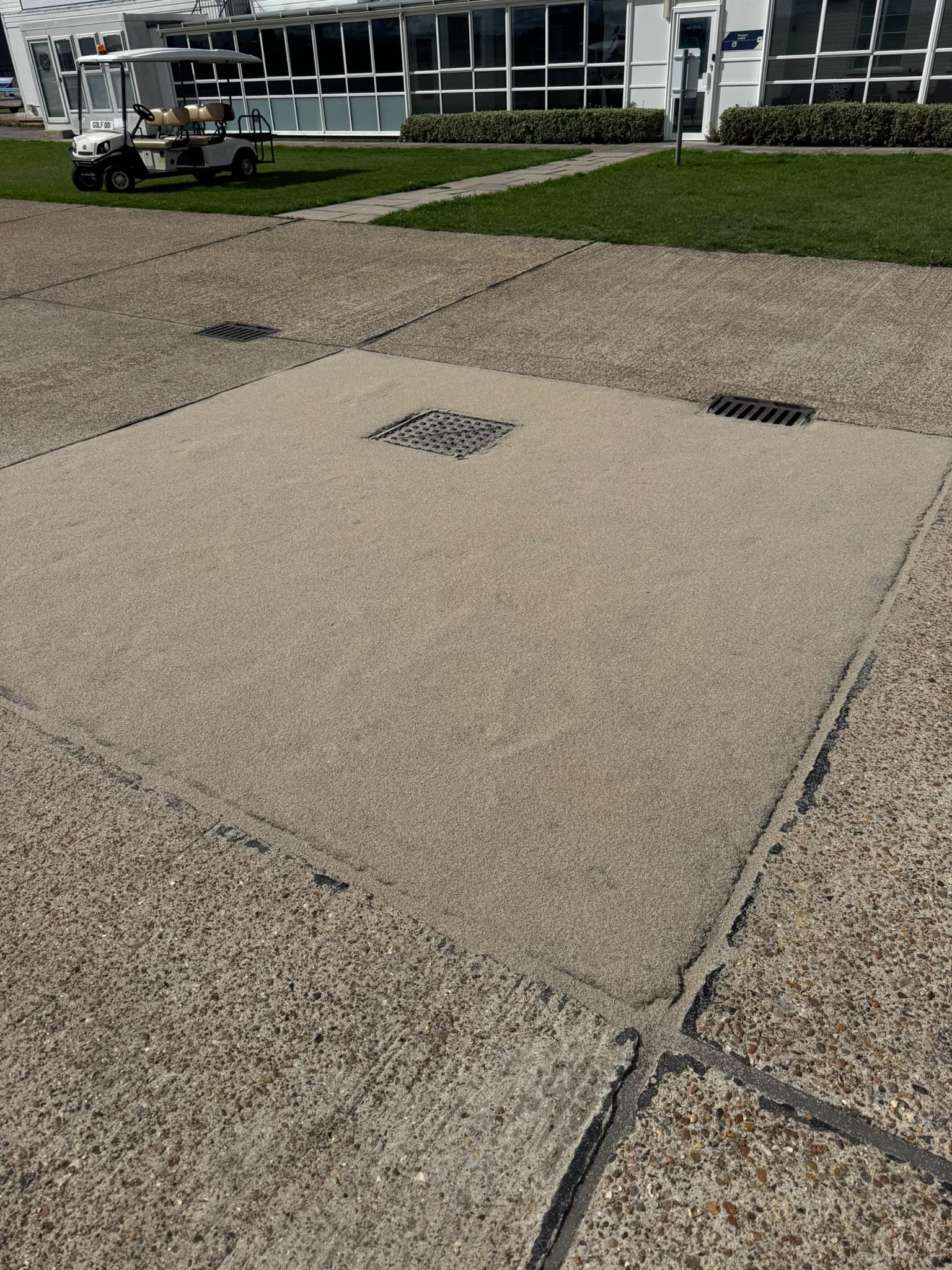 A completed concrete bay repair on an airfield, the new resin and aggregate surface finished flush with the surrounding slabs and the drainage gully reinstated